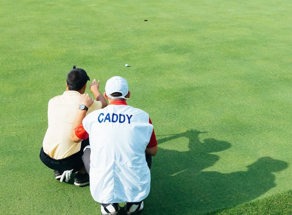 Golfer and caddy reading green 